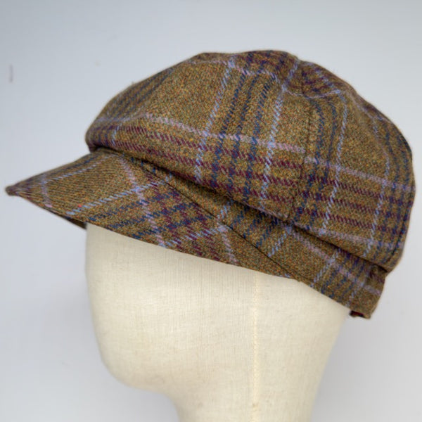 A brown tweed flat cap with a plaid pattern in purple, beige, and brown, displayed on a cream-colored fabric mannequin head against a light gray background.