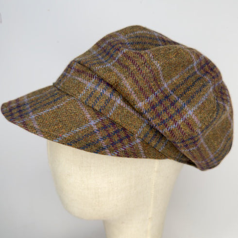 A brown tweed flat cap with a plaid pattern in purple, blue, and beige, displayed on a cream-colored fabric mannequin head against a plain white background.