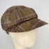 A brown tweed flat cap with a plaid pattern in purple and beige, displayed on a cream-colored mannequin head against a plain white background.