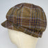 A brown tweed flat cap with a plaid pattern in purple, blue, and beige, displayed on a cream-colored mannequin head against a light gray background.