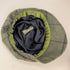 A top-down view of a classic flat cap in a green and blue plaid tweed pattern, featuring a dark navy satin interior and a green fabric trim around the crown.