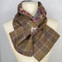 A folded plaid scarf draped on a cream-colored mannequin torso. The scarf features a brown, purple, and beige plaid pattern on the exterior, with a multicolor paisley pattern lining visible at the top edge.